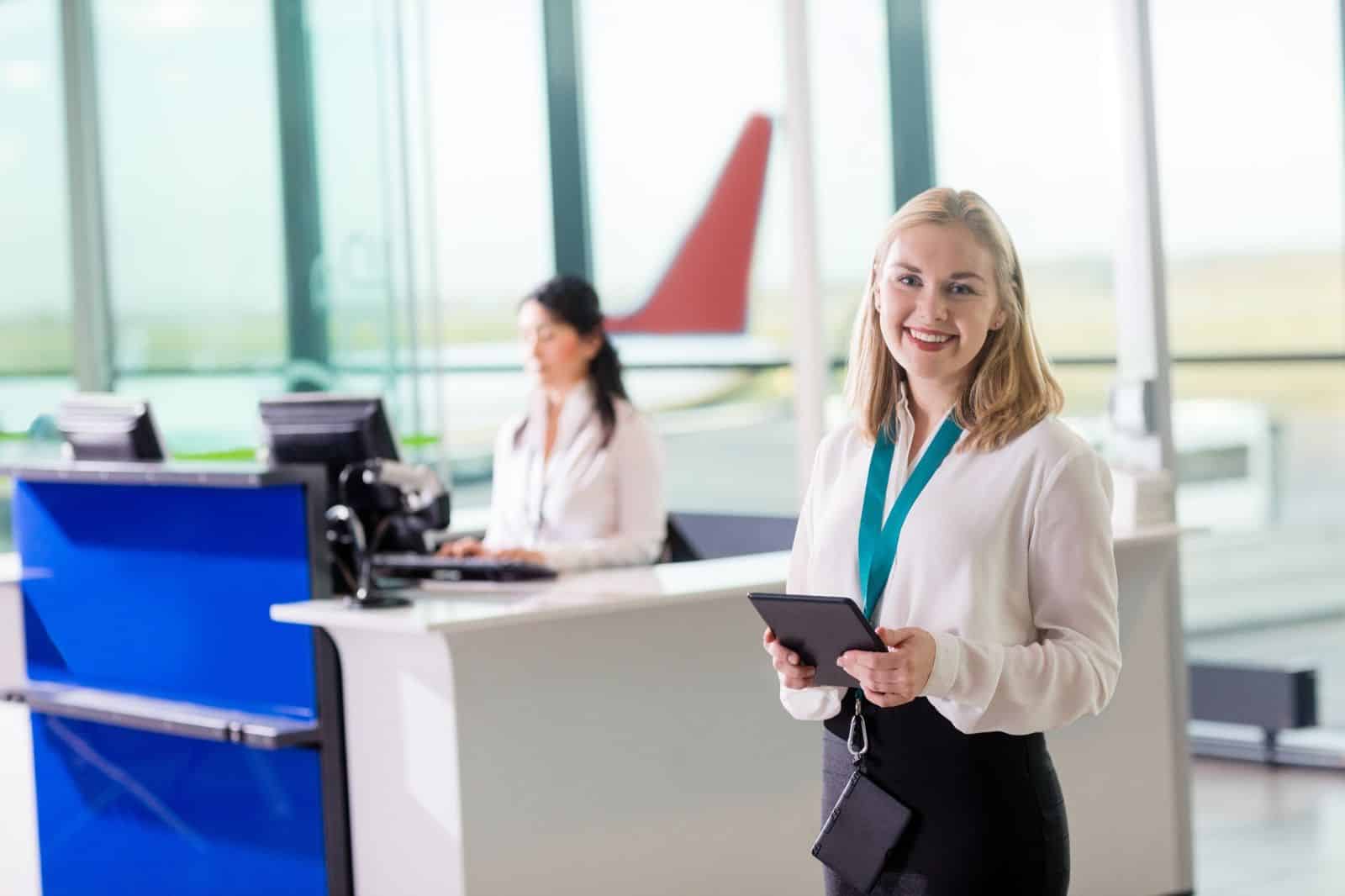 Airport customer service representative holding a tablet at a check-in counter
