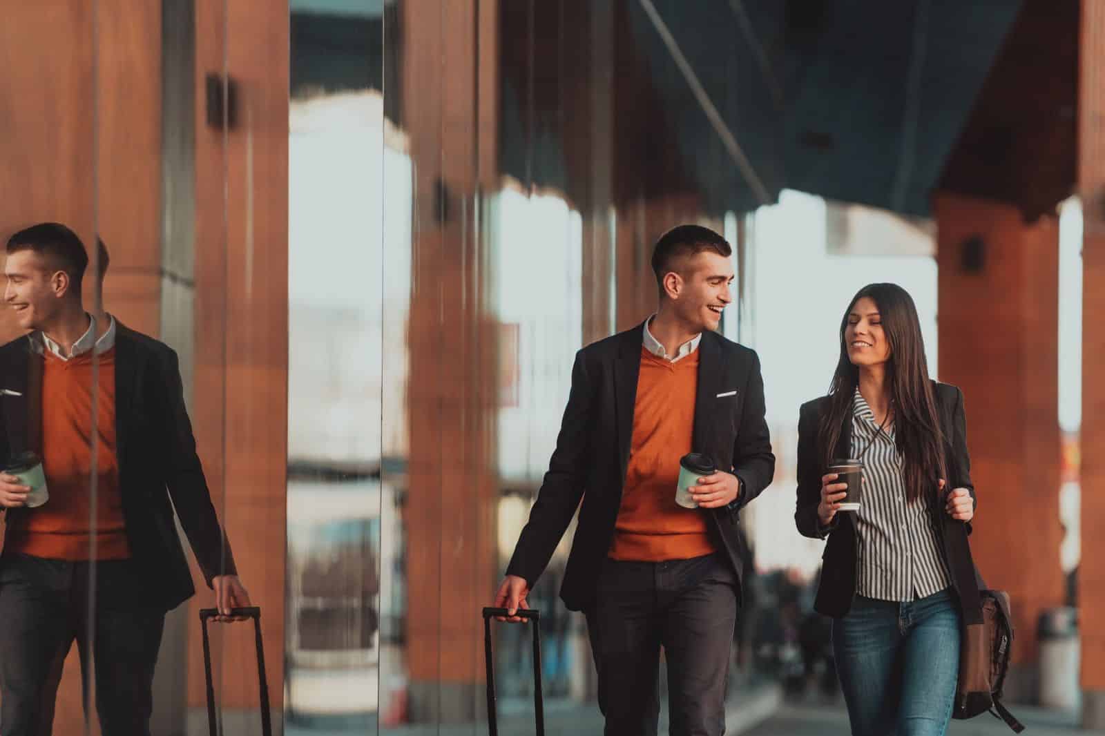 Business travelers walking with luggage and coffee outside a modern airport terminal