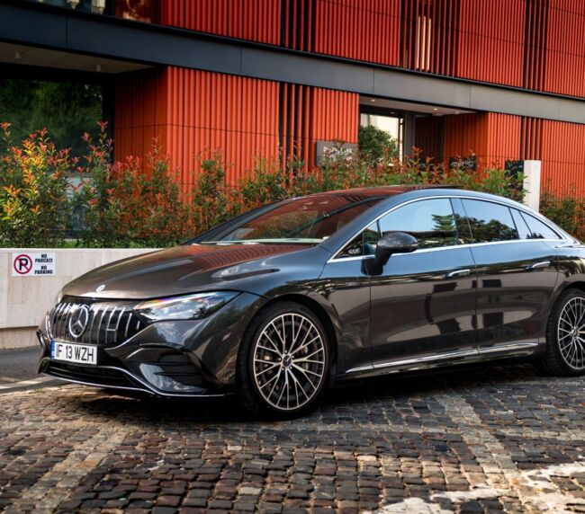 Black Mercedes luxury sedan parked on cobblestone street near modern architecture
