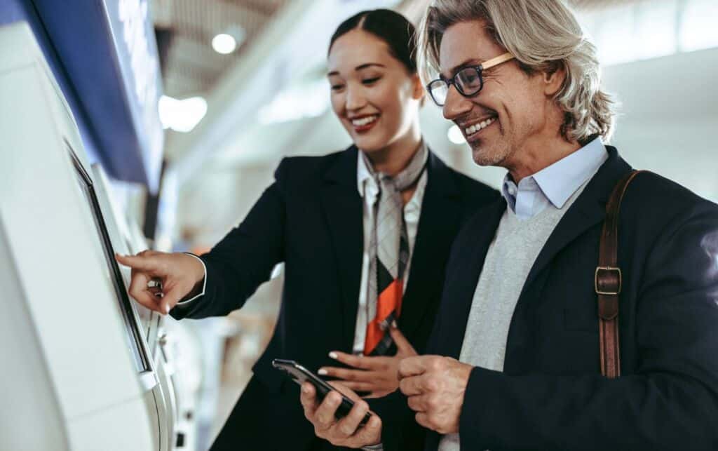 Traveler using a self-service check-in kiosk with assistance from airport staff
